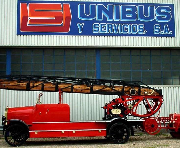 Camión de bomberos histórico con escalera de madera frente a la nave de Unibus y Servicios